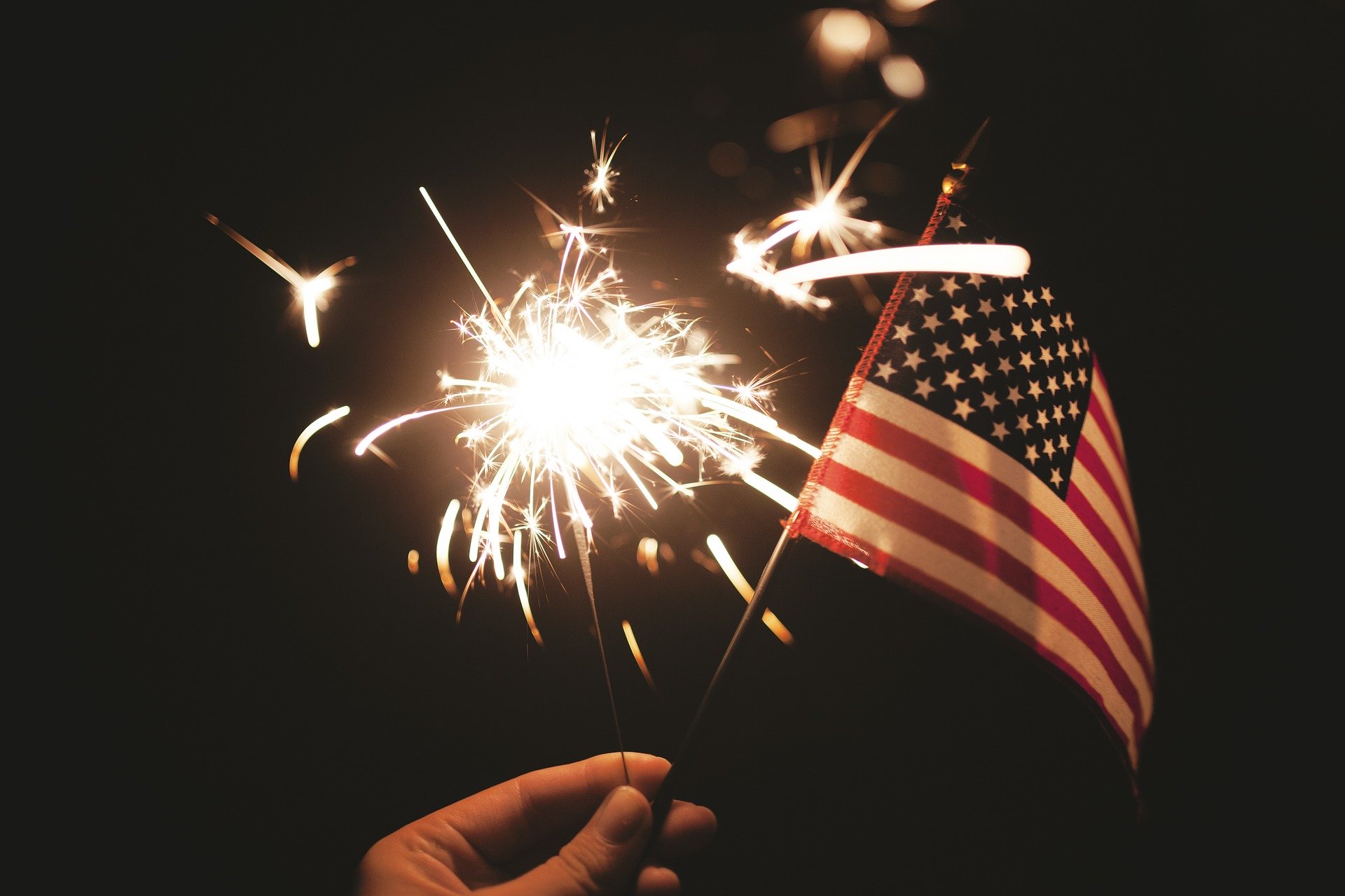 hand holding sparkler and american flag in dark