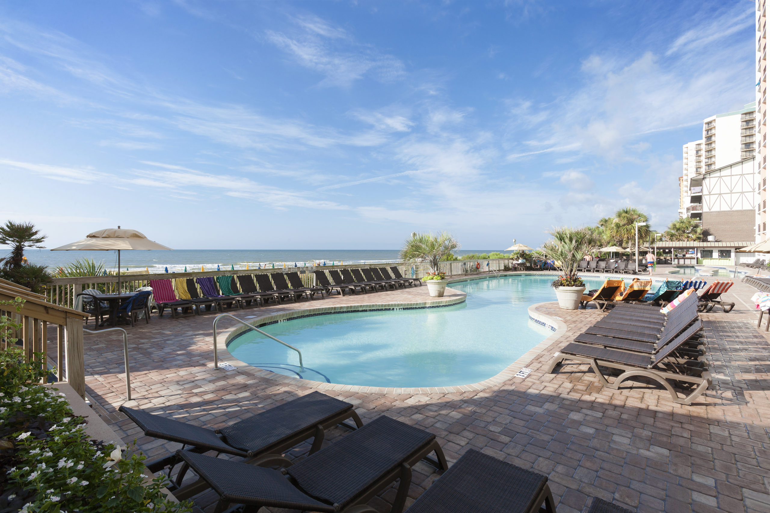 A pool area with lounge chairs and a beach in the background